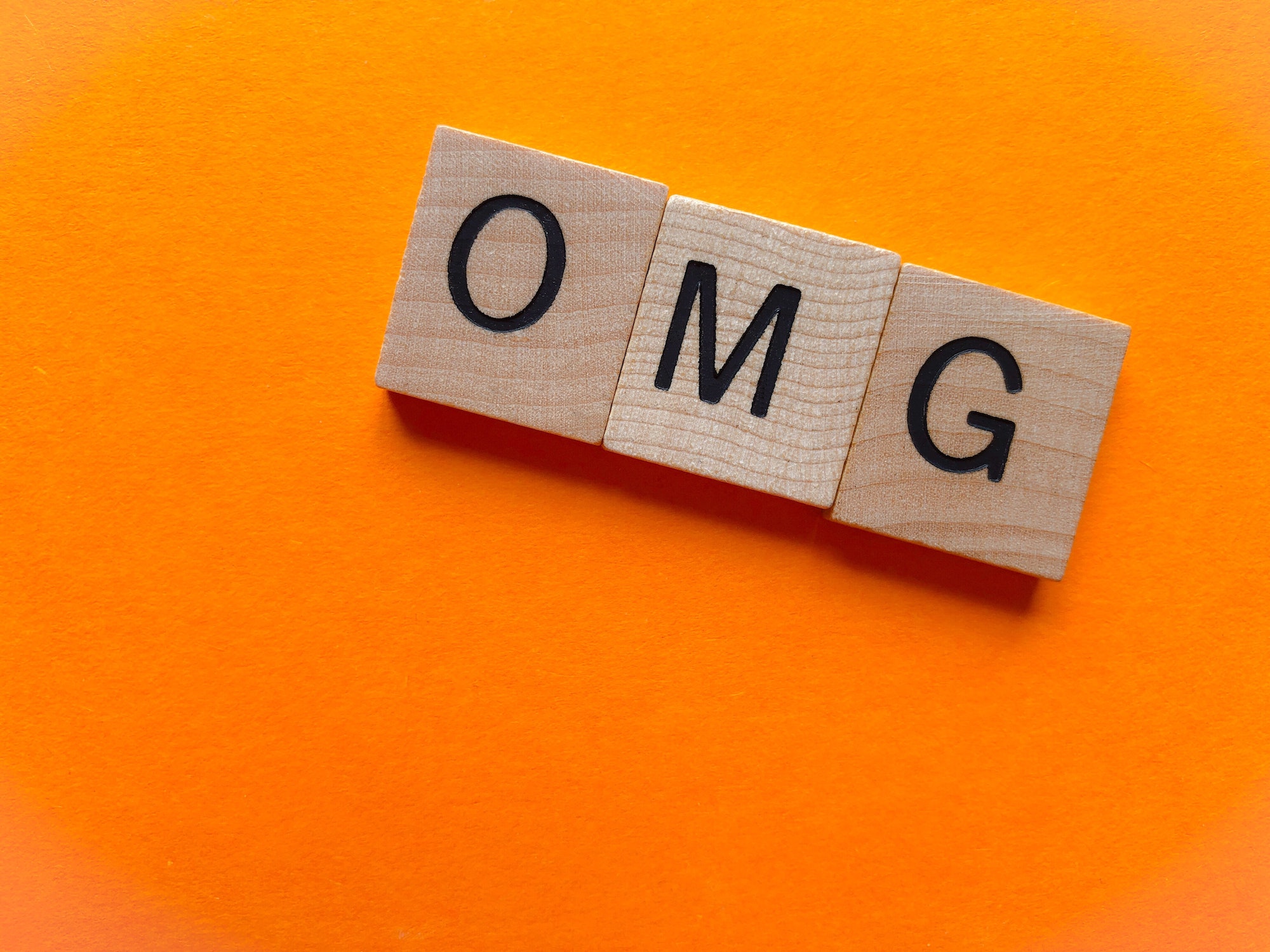 Internet Slang, OMG, Oh My God, in wooden letters on an orange background with copy space
