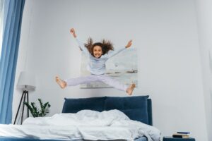 happy little african american girl in pajamas jumping on bed