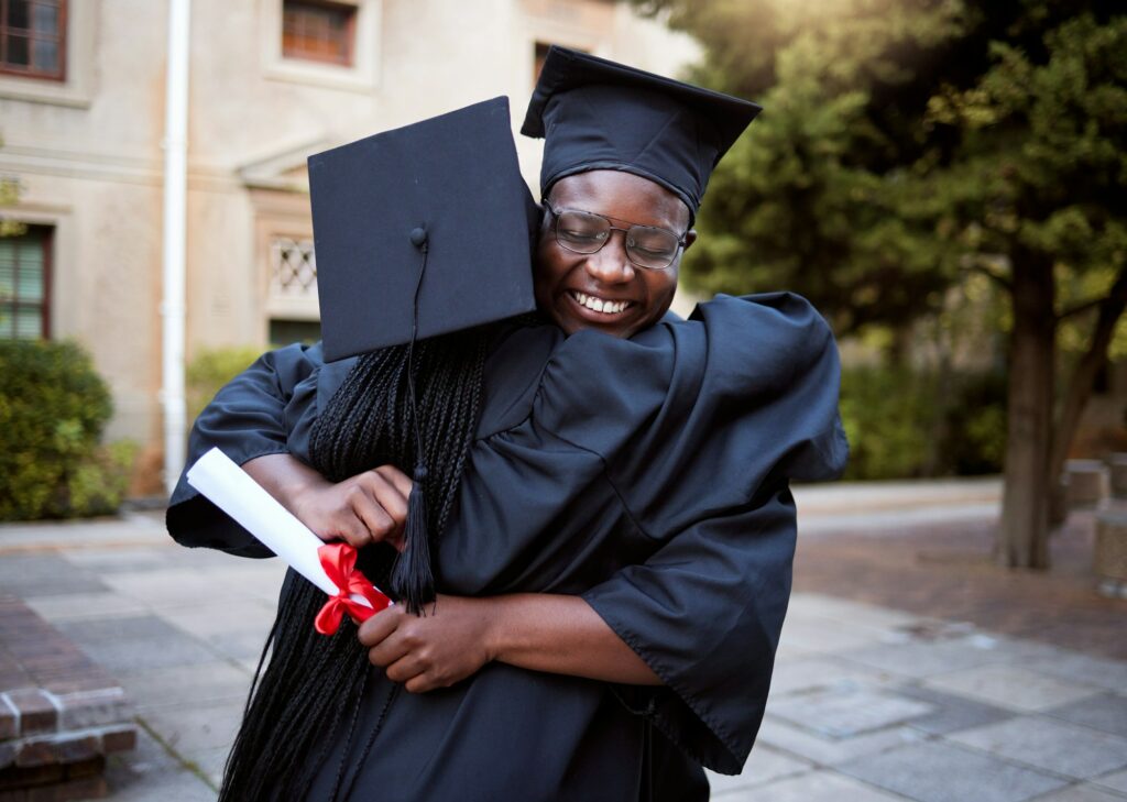 Black people, hug and celebration in graduation ceremony, university degree success or school diplo