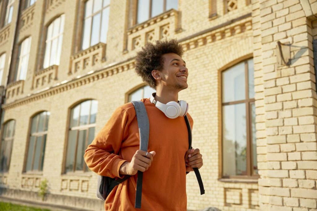 Exited teenage student walking among buildings of university campus