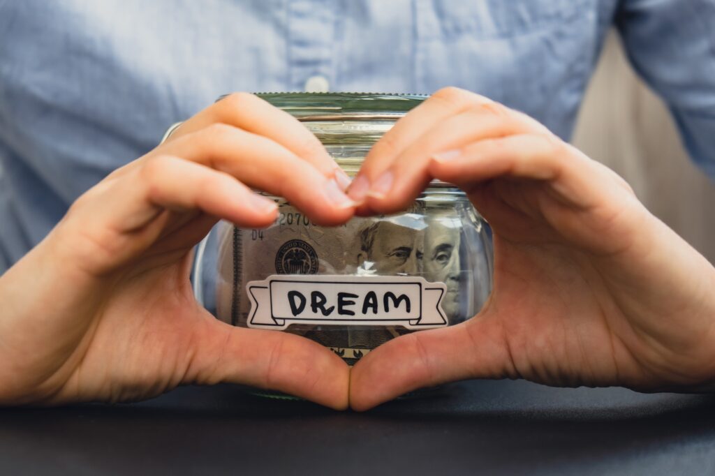 Unrecognizable woman showing heart sign Saving Money In Glass Jar filled with Dollars banknotes