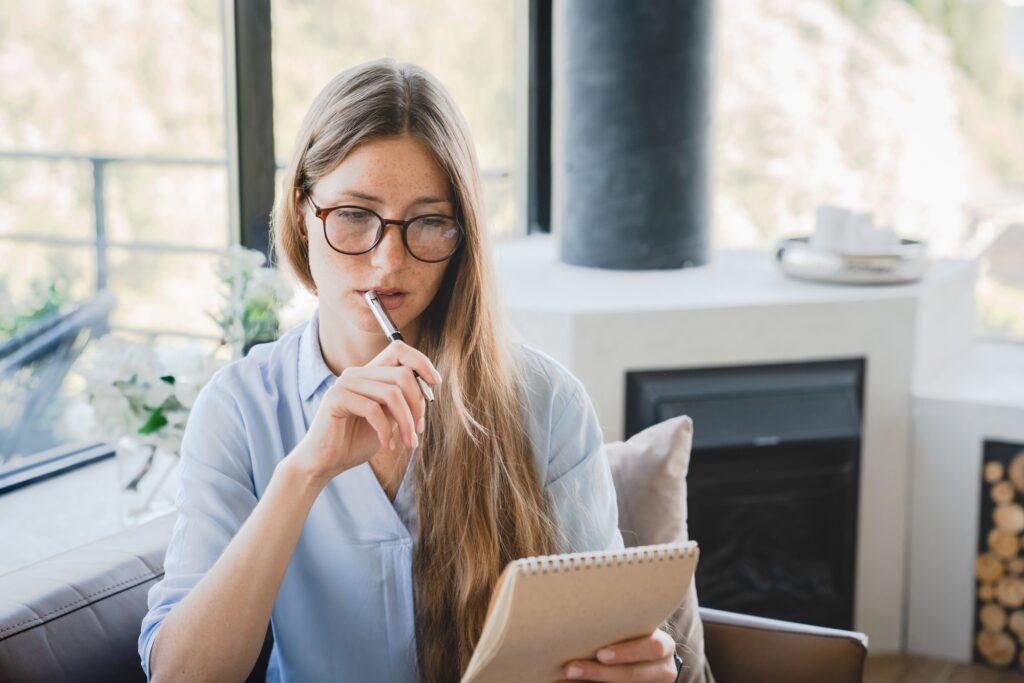 Young pensive woman making to-do list and taking notes at home.