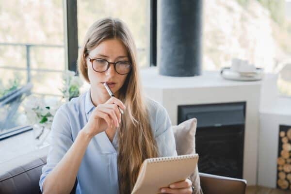 Young pensive woman making to-do list and taking notes at home.
