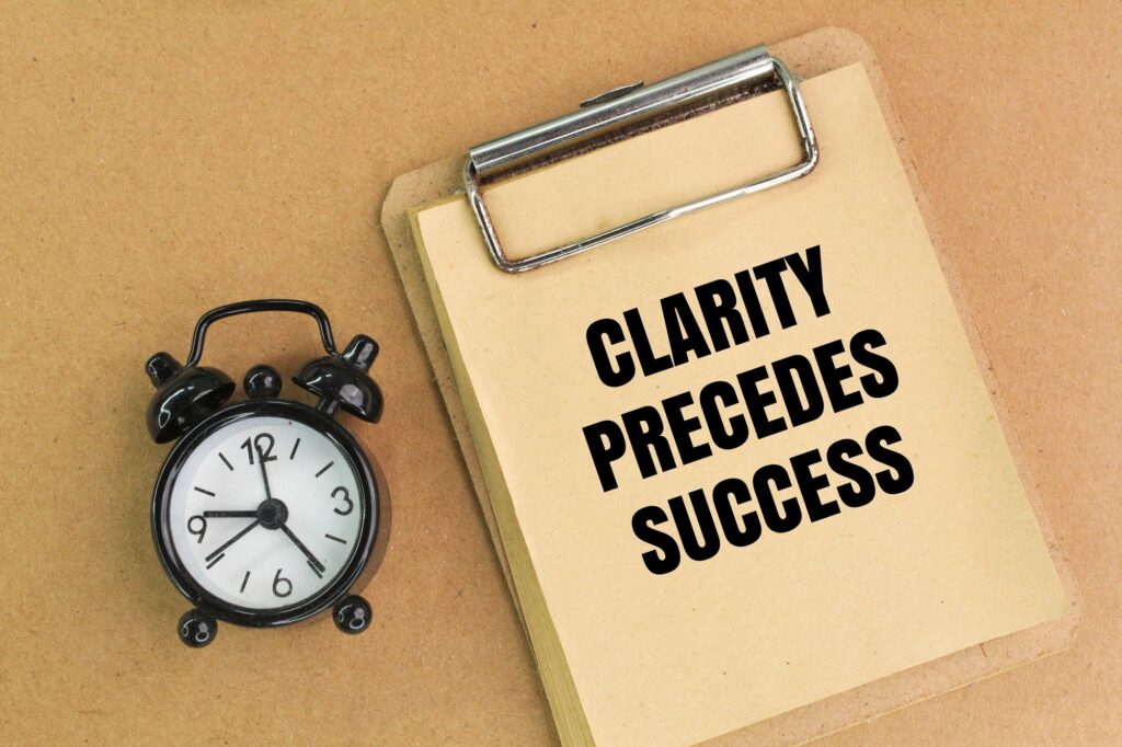 bell clock and paper board with the words Clarity, Precedes, Success.