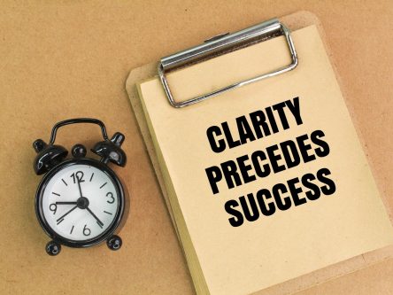 bell clock and paper board with the words Clarity, Precedes, Success.