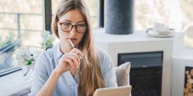 Young pensive woman making to-do list and taking notes at home.