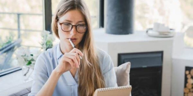 Young pensive woman making to-do list and taking notes at home.